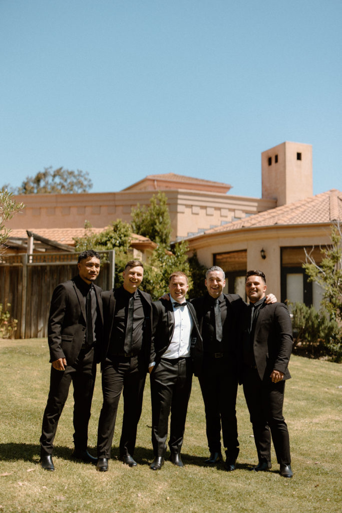 Groom with his groomsmen all dresses in black suits standing together smiling