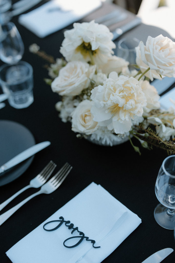 Wedding table details, featuring white flowers on a black tablecloth with a black place card