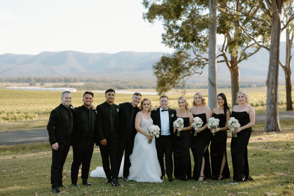 Wedding party with bride and groom, groomsmen and bridesmaids, wearing black dresses with black suits 