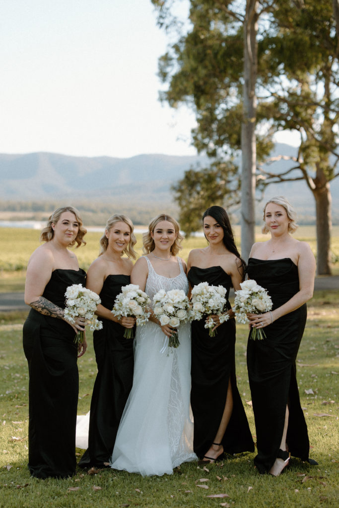 Bride with bridesmaids, with bridesmaids wearing black dresses holding white bouquets
