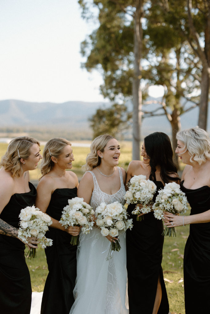 Bride with bridesmaids, with bridesmaids wearing black dresses holding white bouquets, laughing 

