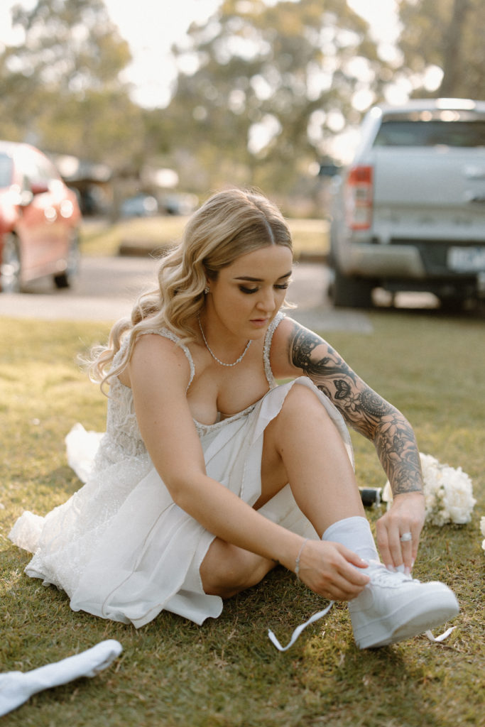 Bride sitting on the grass changing into white sneakers