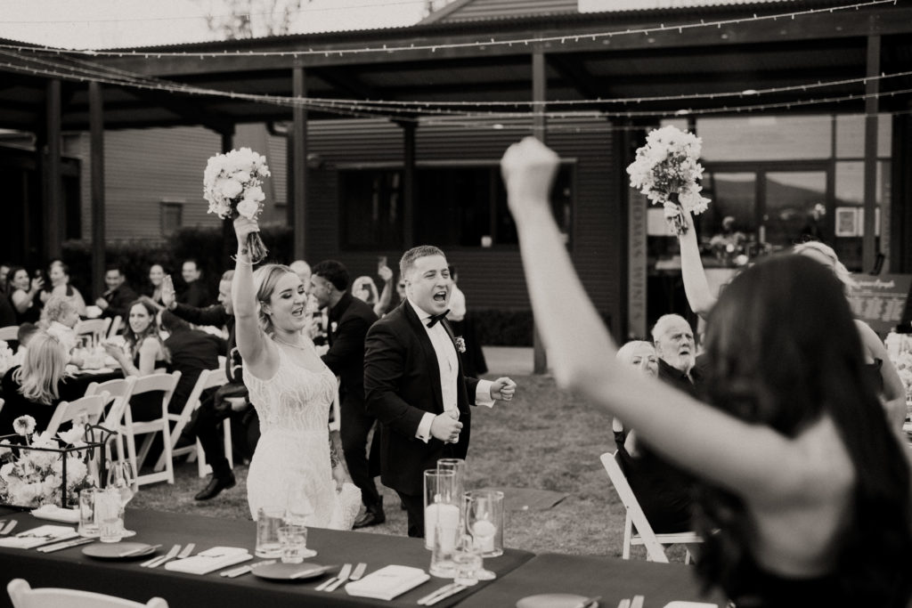 Bride and groom entering their reception with their arms up in the air cheering