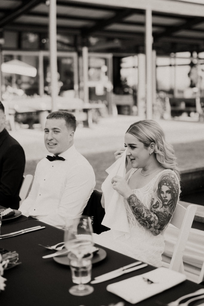 Bride and groom sitting at their bridal table, while the bride wipes away tears with napkin